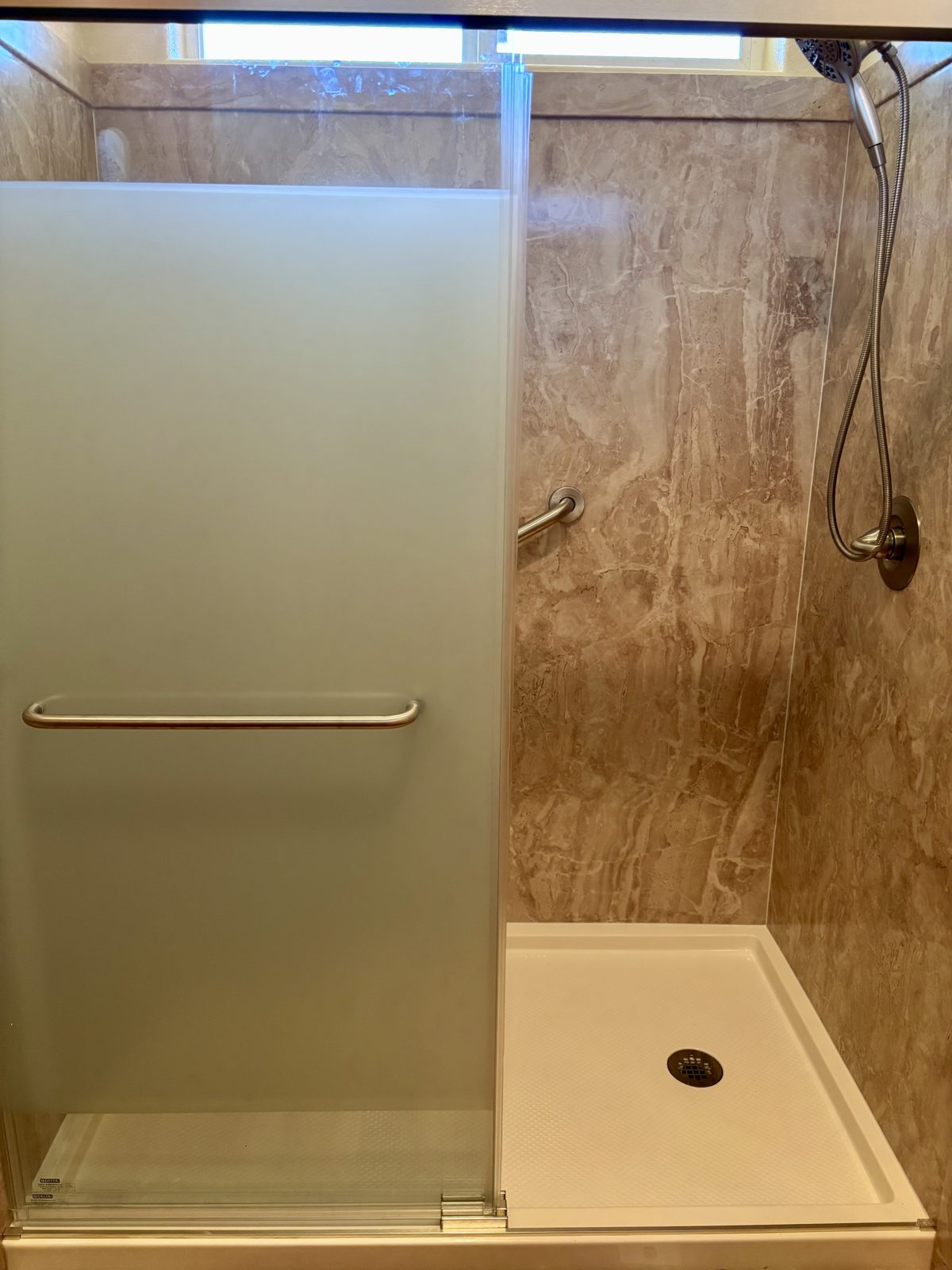 After: new walk-in shower with marble-look walls, low-profile shower base, and frosted sliding glass door